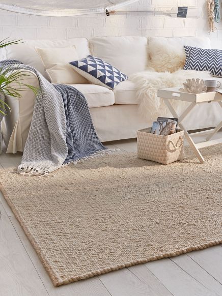Beigefarbener Teppich auf Holzboden, Sofa mit Kissen und Decken, Couchtisch mit Dekorationen im Raum.