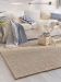 Beigefarbener Teppich auf Holzboden, Sofa mit Kissen und Decken, Couchtisch mit Dekorationen im Raum.