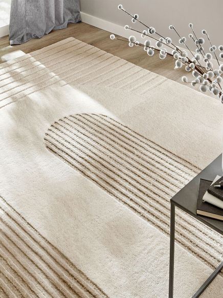 Beigefarbener Teppich mit geometrischen Streifen und Bögen, im Wohnzimmer auf Holzboden.