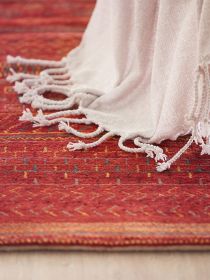 Roter Teppich mit geometrischem Muster, weiße Decke mit Fransen liegt darauf.