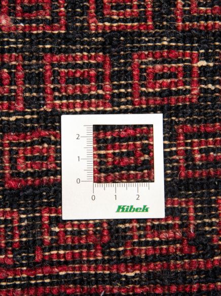 Maßstab misst rote und schwarze gewebte Textur mit geometrischem Muster, Text „Kibek“.