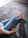 Person sitzt auf grauem Teppich und hält Kaffeetasse, trägt blaue Jeans und rosa Pullover.