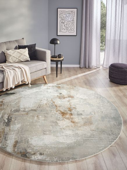 Runder Teppich liegt auf Holzboden vor grauem Sofa mit Kissen und Tagesdecke im Wohnzimmer.