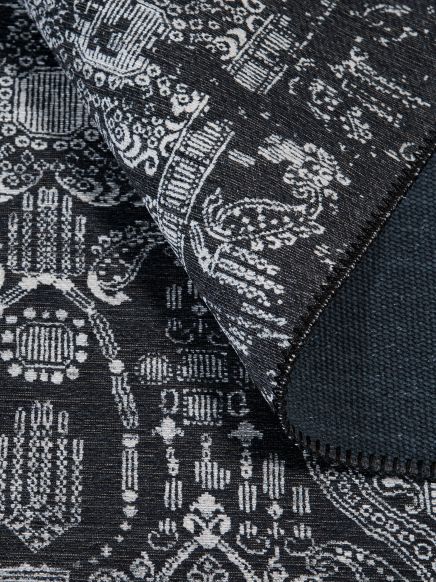 Teppich zeigt weiße ornamentale Muster auf schwarzem Grund, Ecke ist hochgeklappt.