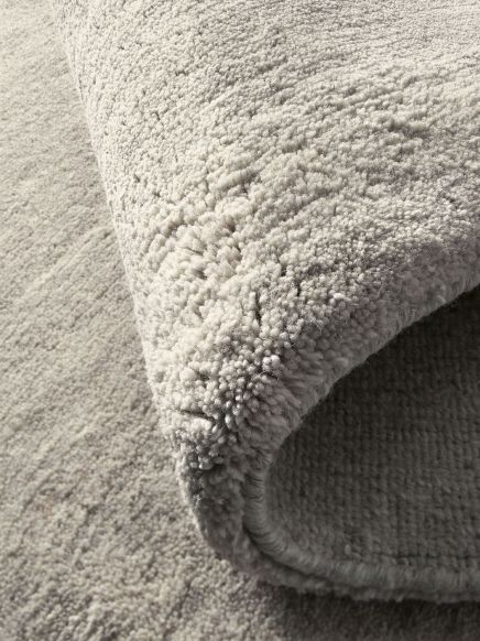 Beiger Teppich wird auf Teppichboden mit ähnlicher Farbe aufgerollt, Nahaufnahme der Textur.