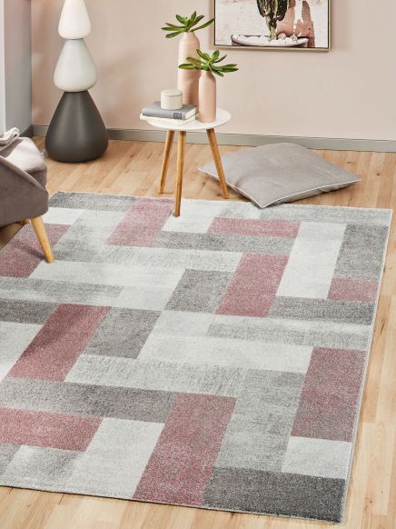 Tisch mit Pflanzen und Büchern steht auf kariertem Teppich im Wohnzimmer mit Sofa und Kissen.