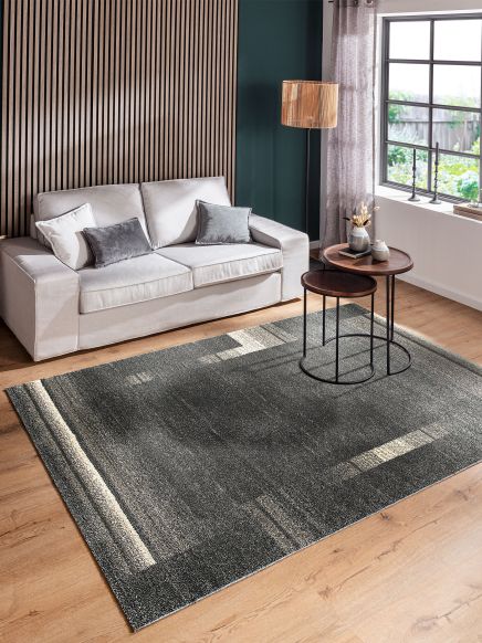 Beiger Sofa sitzt vor holzvertäfelter Wand, neben zwei runden Couchtischen, großem Fenster und Teppich.