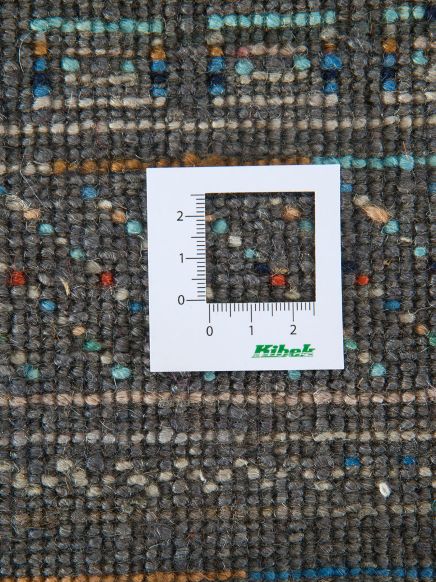 Maßstab misst Teppichstruktur mit bunten Fäden auf grauem Hintergrund, Kibek-Logo sichtbar.
