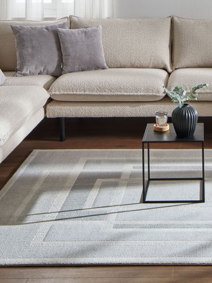 Ecksofa mit zwei Kissen, schwarzer Beistelltisch mit Glas und Vase auf gemustertem Teppich.