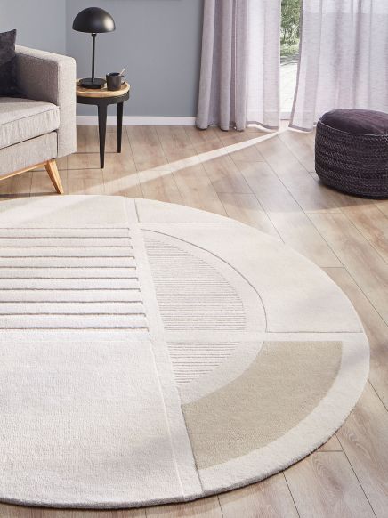 Runder Teppich mit geometrischem Muster liegt auf Holzboden neben grauem Sofa und Beistelltisch.