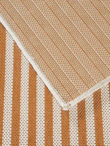 Zwei gewebte Teppiche liegen übereinander, orange-weiße Streifen unten, beige Muster oben.