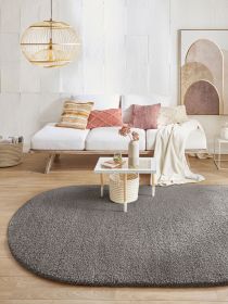Grauer Teppich liegt vor Sofa mit Kissen, Tisch mit Vase und Lampe in hellem Wohnzimmer.