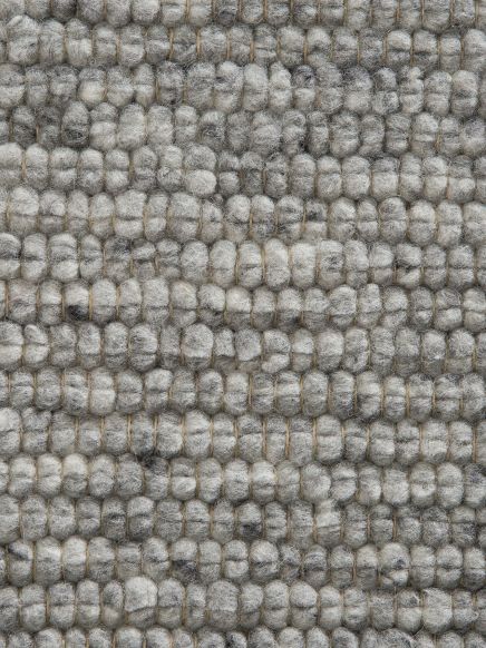 Nahaufnahme von grauen Wollfasern, die in kleinen, dichten Kugeln auf einem Teppich gewebt sind.