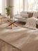Helles Wohnzimmer mit grauem Sofa, braunem Kissen, Decke, Pflanzen und rundem Glastisch.
