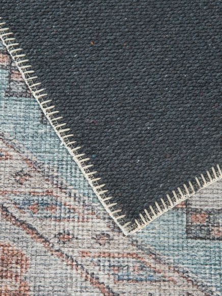 Teppich zeigt Rückseite mit Naht, liegt auf gemustertem Boden mit blauen und braunen Tönen.