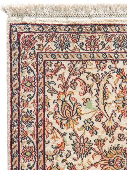Teppich zeigt florale Muster in Rot, Blau und Beige mit Fransen am Rand, Nahansicht.