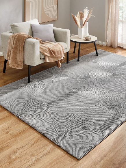 Sessel mit Decke und Kissen steht neben rundem Beistelltisch mit Vase und Tasse auf Teppich im Zimmer.