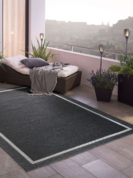 Dunkler Teppich auf Balkon mit Liege, Pflanzen, Laternen und Aussicht auf neblige Stadtsilhouette