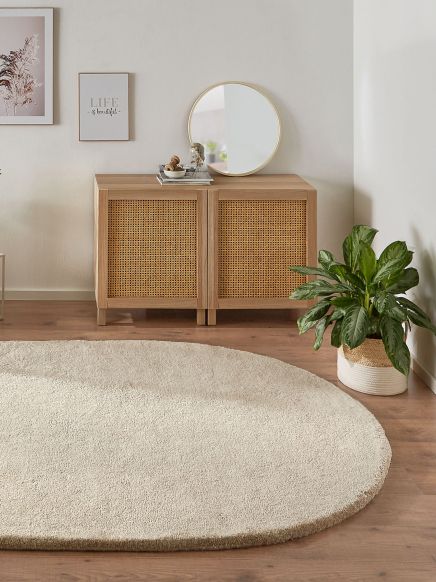 Runder Teppich liegt vor Sideboard mit rundem Spiegel, Wandbildern und Pflanze im hellen Raum.