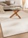 Runder Couchtisch mit Glasplatte steht auf hellem Teppich vor beige Sofa mit Kissen und Decke.