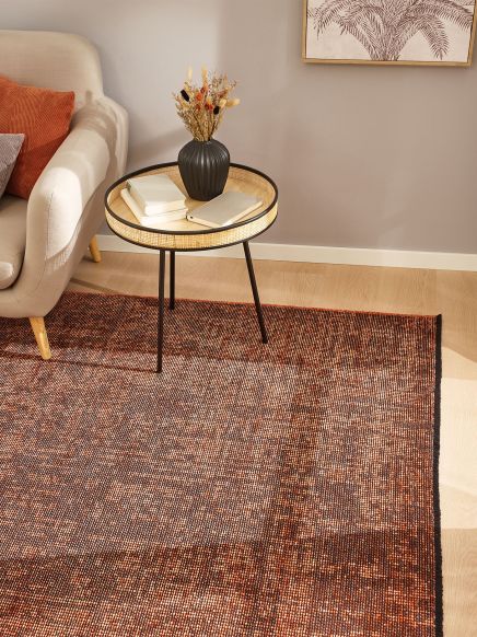 Tisch mit Vase und Büchern neben Sofa im Wohnzimmer auf gemustertem Teppich neben Wandbild