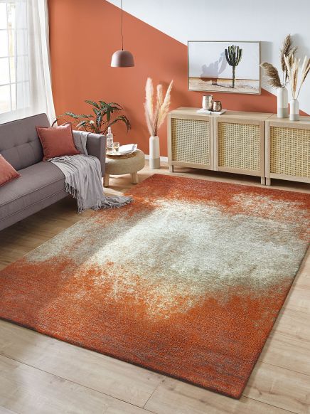 Moderner Teppich liegt auf Holzfußboden in Wohnzimmer mit Sofa, Kommode und Deko.