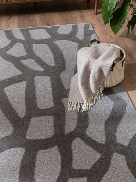 Korb mit Decke liegt auf grauem Teppich mit abstraktem Muster im Raum mit Holzboden.