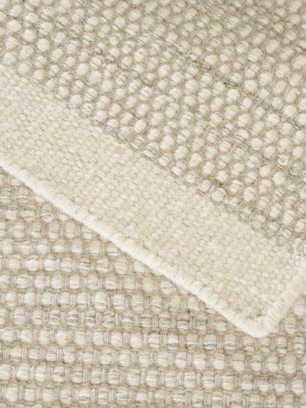 Teppich zeigt Struktur mit dicken, gepolsterten Reihen in neutralen Beigetönen, Nahaufnahme.