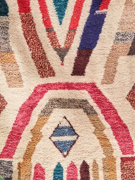 Teppich zeigt abstrakte geometrische Muster in Rot, Blau, Braun und Beige.