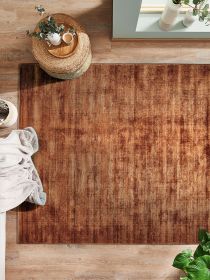 Braun gemusterter Teppich liegt auf Holzboden mit Pflanzen, Körben und Decke daneben.