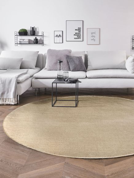 Beiger runder Teppich liegt vor weißem Sofa mit Kissen, Couchtisch mit Karaffe und Glas im Wohnzimmer.