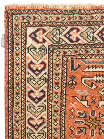 Ecke eines Teppichs mit geometrischem Muster in Rot, Beige, Blau und Schwarz auf weißem Hintergrund.