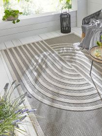 Teppich mit Linienmuster liegt auf weißem Boden Sofa mit Decke und Tisch mit Getränken daneben.