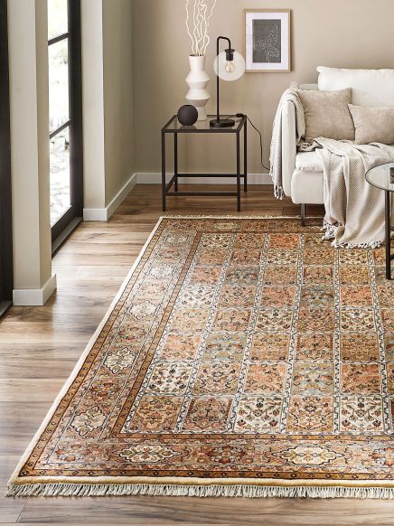 Orientteppich liegt auf Holzboden, neben Sofa mit Decke und Kissen sowie Beistelltisch mit Lampe und Vase.