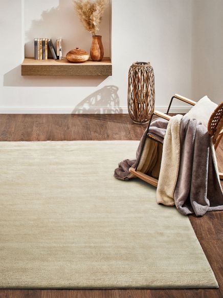 Beiger Teppich auf Holzboden, darauf ein Stuhl mit Decken; Regal mit Vasen und Büchern an der Wand