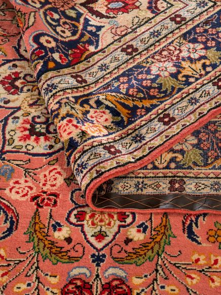 Orientteppich zeigt florale Muster, wird an Ecke hochgeklappt, bunte Detailmuster auf rosa Grund