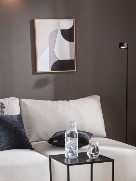 Glaskaraffe mit Eis und Wasserglas stehen auf kleinem schwarzen Tisch vor hellem Sofa und abstraktem Bild.