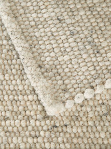 Mehrere gewebte Teppiche mit kugelförmiger Struktur in hellen Beige- und Grautönen übereinandergelegt.