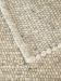 Mehrere gewebte Teppiche mit kugelförmiger Struktur in hellen Beige- und Grautönen übereinandergelegt.