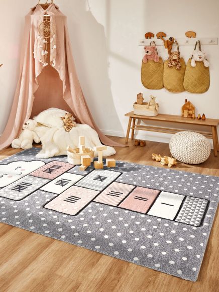 Kinderteppich mit Hüpfenmuster und Spielklötzen auf Holzboden in Spielzimmerecke mit Kuschelhöhle.