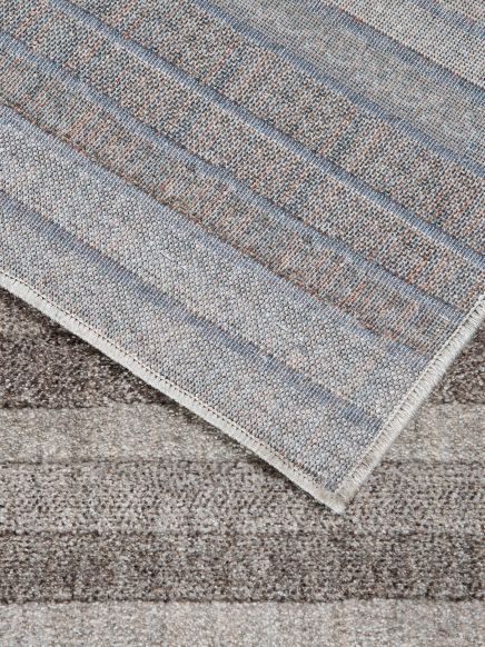 Teppich zeigt von unten genähte Ecke mit grauen und beigen Streifen auf Teppichboden.