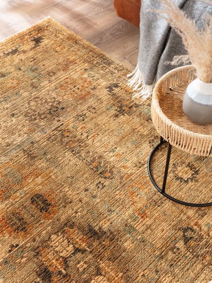 Teppich liegt auf Holzboden, daneben runder Beistelltisch mit Vase und Grau-Decke.