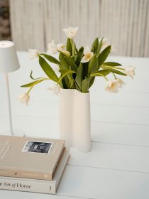 Vase mit weißen Tulpen steht auf weißem Tisch neben zwei gestapelten Büchern und kleiner Lampe.