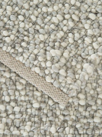 Kuscheliger, grob gewebter Teppich mit beige-grauen Flocken und beigem Saumrand.