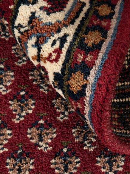 Orientteppich zeigt Muster mit roten, weißen, blauen und braunen Farben, Teil ist umgeklappt.