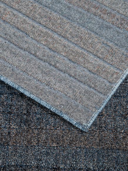Teppich liegt auf einem anderen Teppich, beide mit unterschiedlichen texturierten graublauen Mustern.