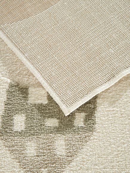 Teppich liegt auf einem Teppich mit geometrischem Muster, Ecke des oberen Teppichs nach oben gebogen.