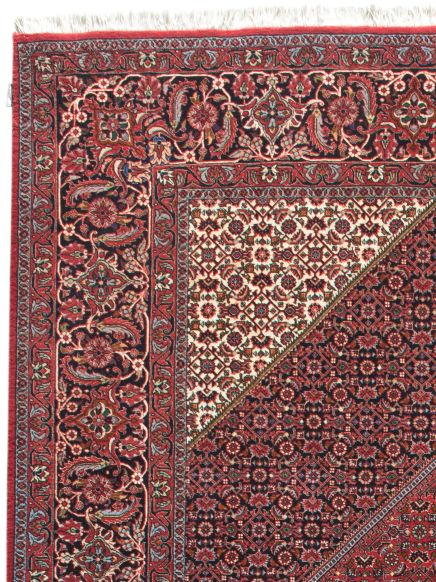 Teppich mit komplexem floralem Muster in Rot, Blau und Weiß, Ecke umgeklappt.