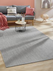 Grauer Teppich liegt unter rundem Couchtisch mit Vase und Glas vor Sofa mit roten Kissen im Wohnzimmer.