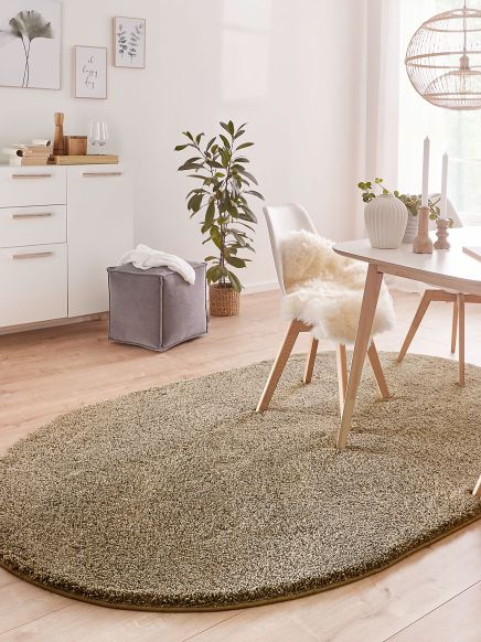 Ovaler Teppich liegt unter Stuhl mit Fellbezug und Esstisch in hellem Wohnzimmer.